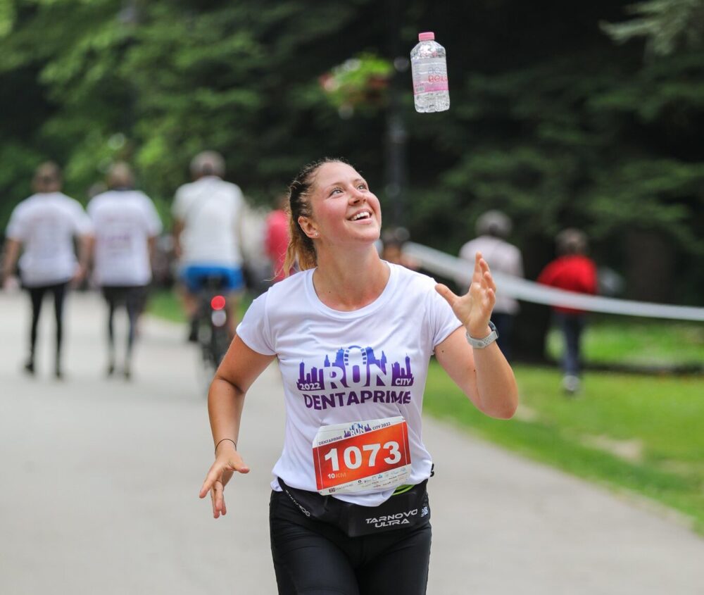 бягащо момиче на маратон dentaprime run city, което подхвърля бутилка вода aquabella